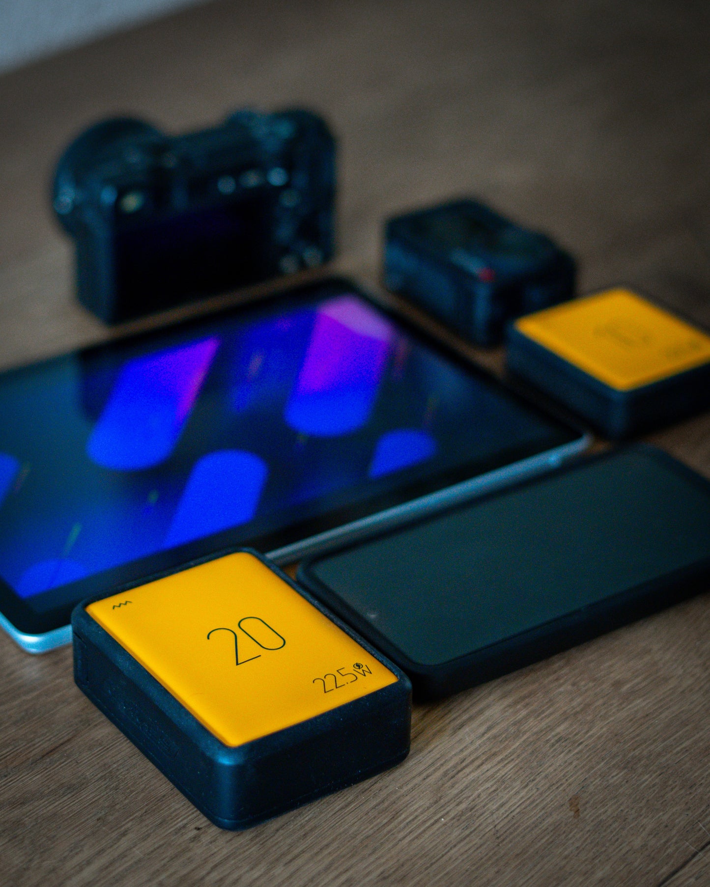 Camera, smartphone, and yellow device on a wooden surface
