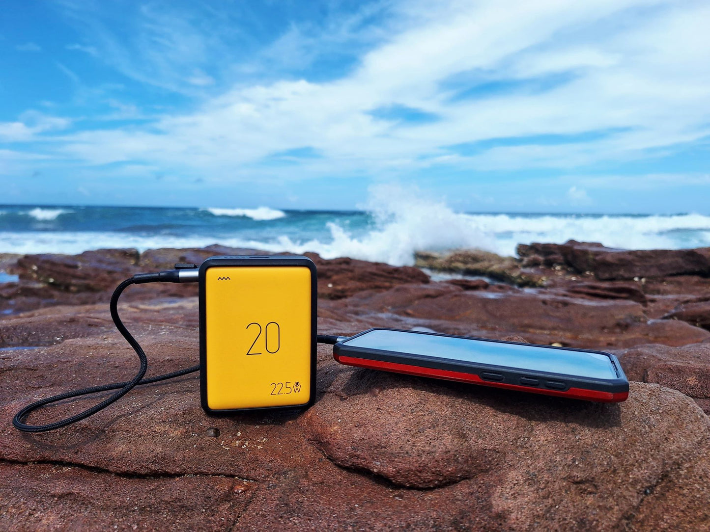 Two electronic devices on a rocky beach with ocean waves in the background